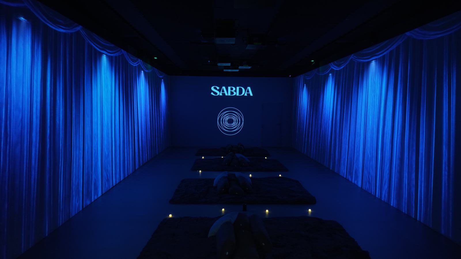 Sala de tallers creatius de SABDA a Barcelona: cortines blaves, estoretes i espelmes a l'espai de projeccions 360